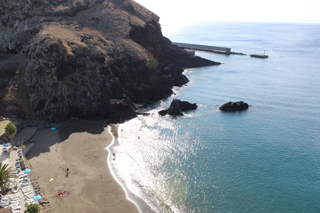 Dark volcanic sand beach below steep cliffs on Madeira, with calm turquoise water